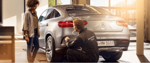 Cinematic photo of a Mercedes employee talking with another person. They are standing next to a grey Mercedes car, and the light is shinning through the window